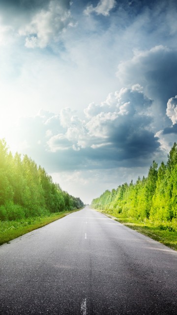 Image gray concrete road between green grass field under white clouds and blue sky during daytime