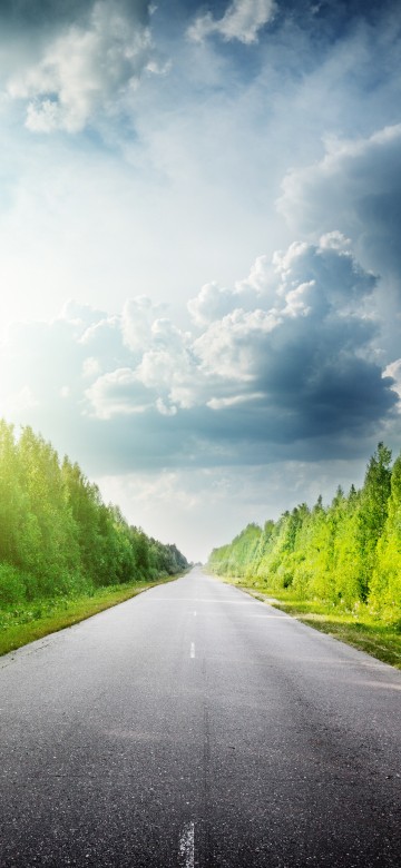 Image gray concrete road between green grass field under white clouds and blue sky during daytime
