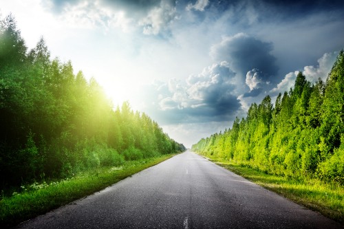 Image gray concrete road between green grass field under white clouds and blue sky during daytime