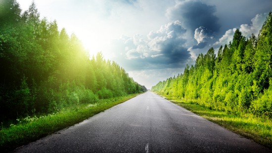 Image gray concrete road between green grass field under white clouds and blue sky during daytime