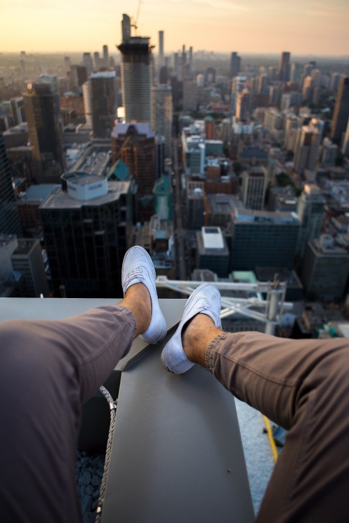 Image person in brown pants and white sneakers sitting on white building during daytime