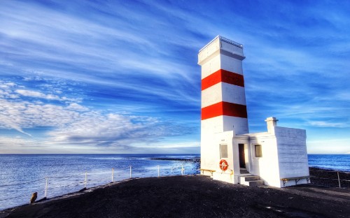 Image white and red lighthouse near body of water during daytime