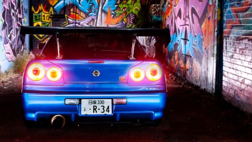 Image purple car parked beside wall with graffiti