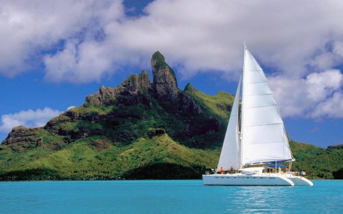 Image white sailboat on sea near green mountain under white clouds and blue sky during daytime