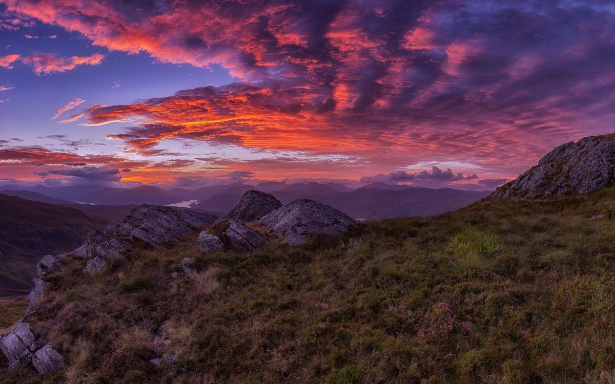 green grass field near mountain under orange and blue sky