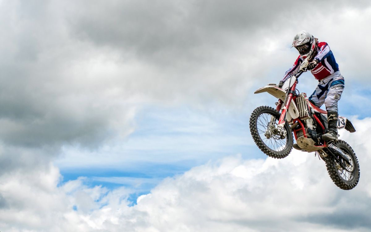 man riding motocross dirt bike doing stunts under white clouds during daytime