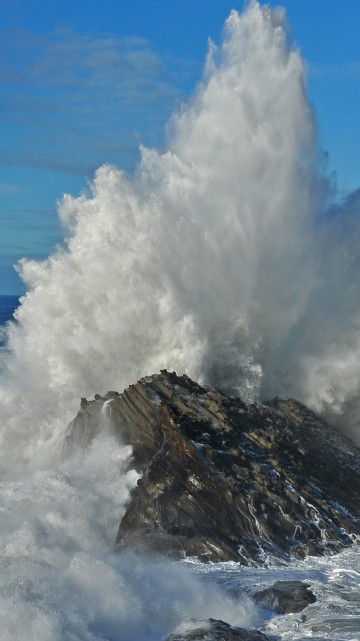 Image ocean waves crashing on brown rock formation under blue sky during daytime