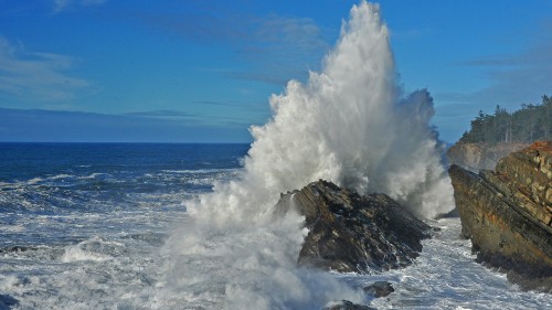 Image ocean waves crashing on brown rock formation under blue sky during daytime