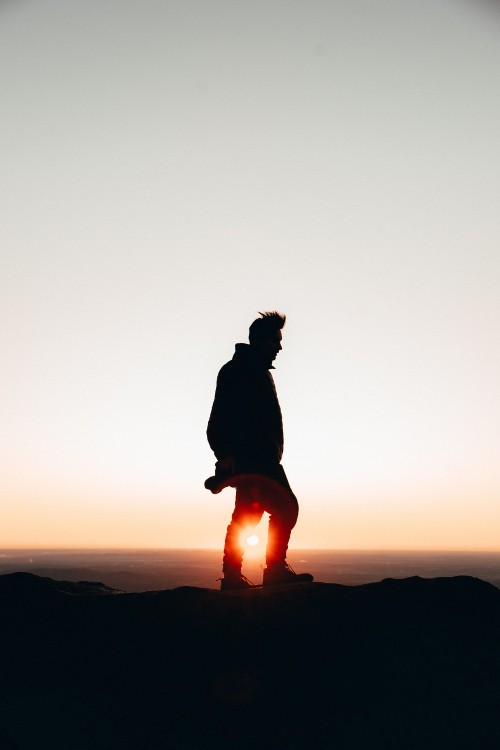 Image silhouette of person sitting on rock during sunset