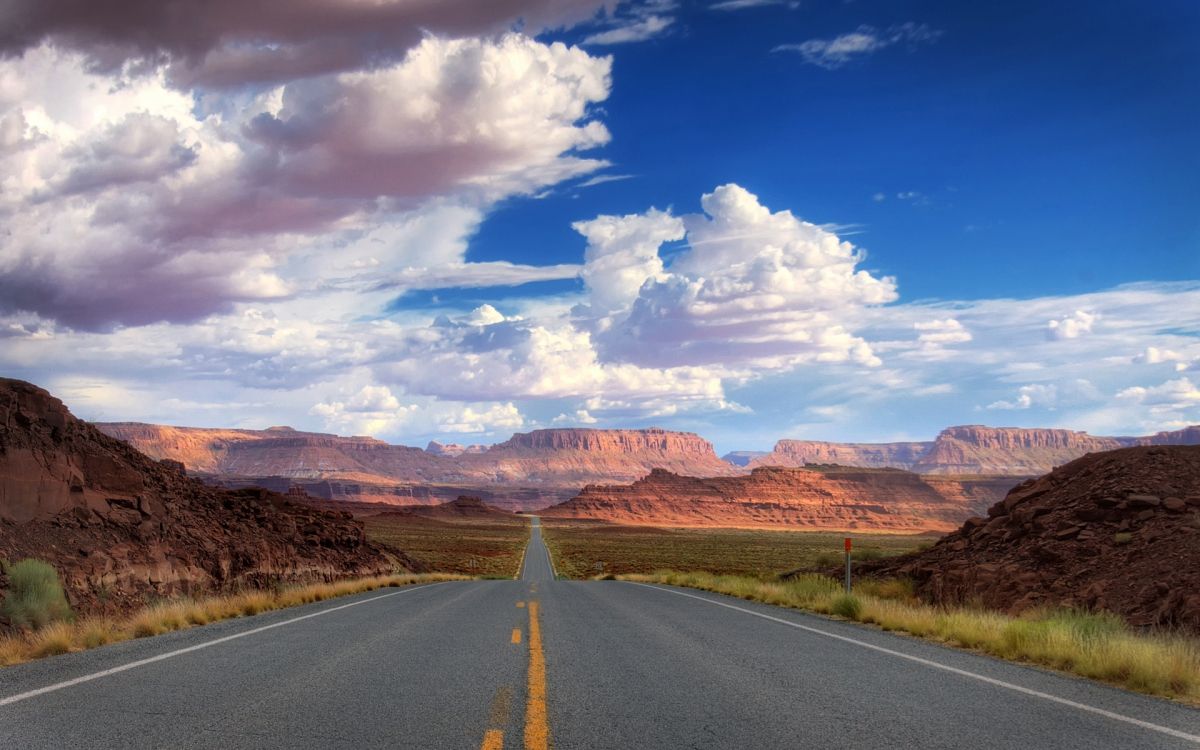 gray asphalt road near brown mountains under blue and white sunny cloudy sky during daytime