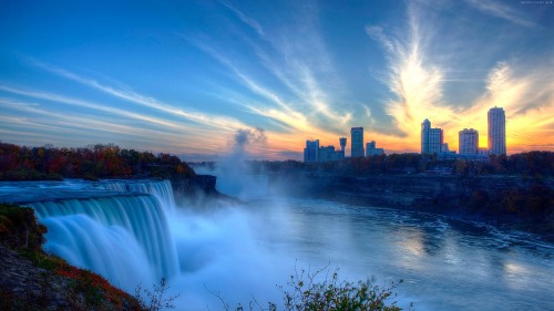 Image water falls near high rise buildings under blue sky during daytime