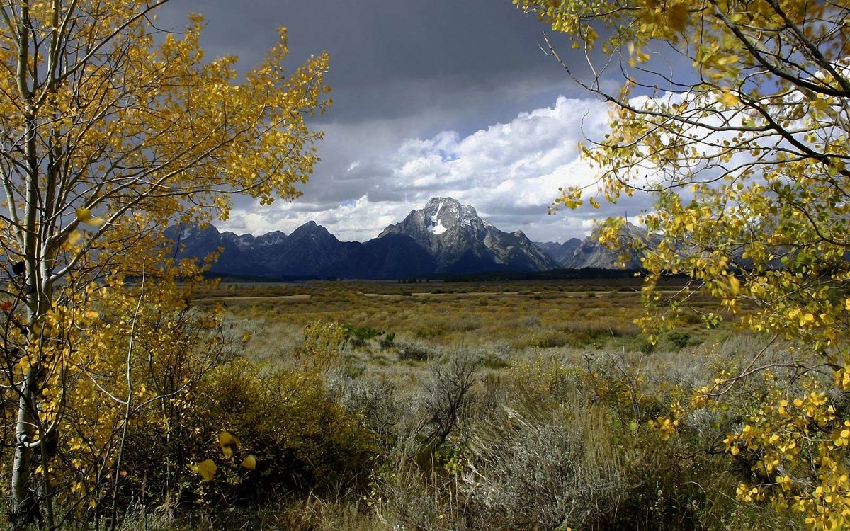 green grass field near mountain under white clouds during daytime