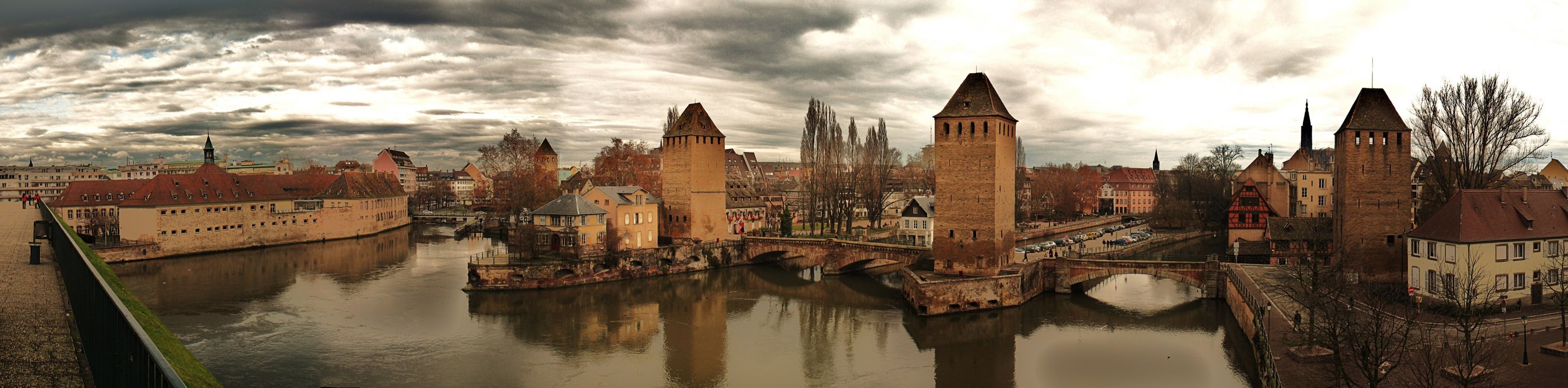 Edificio de Ladrillo Marrón Junto al Río Bajo un Cielo Nublado. Wallpaper in 6657x1648 Resolution