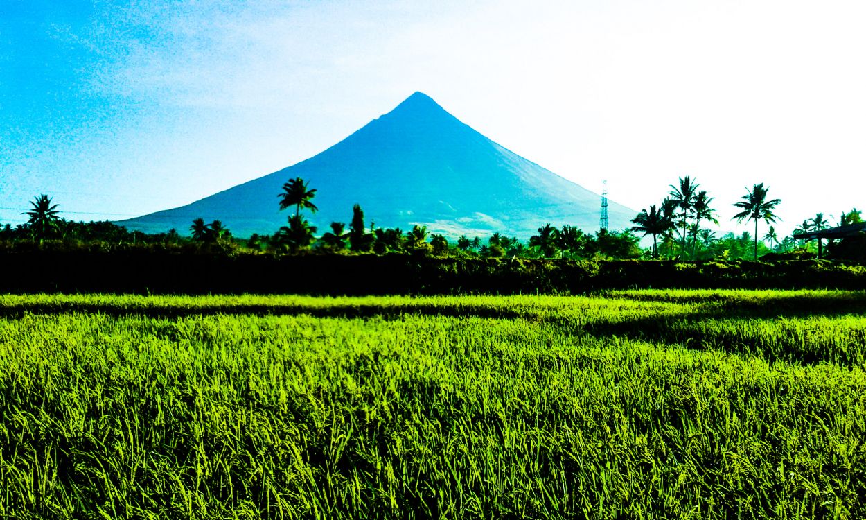 green grass field near mountain under white clouds during daytime