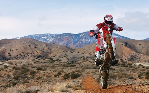 Image man in red and white motocross helmet riding motocross dirt bike on brown field during daytime