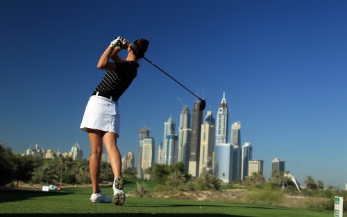 Image woman in black and white stripe shirt and white shorts holding black and silver golf club