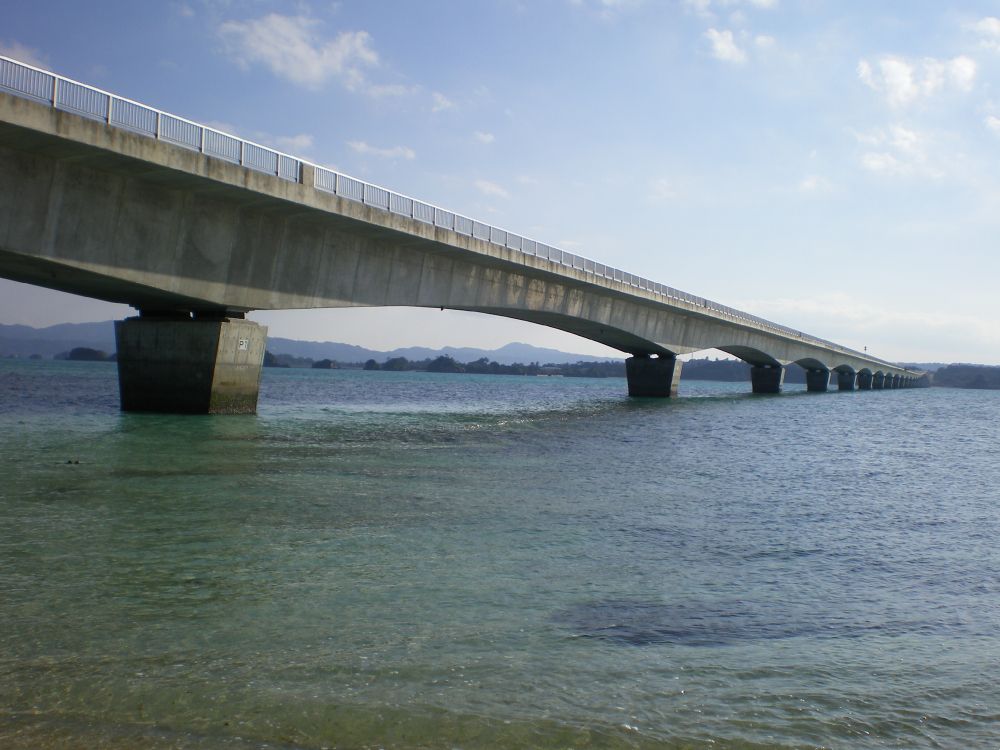 gray concrete bridge over the sea under white clouds during daytime