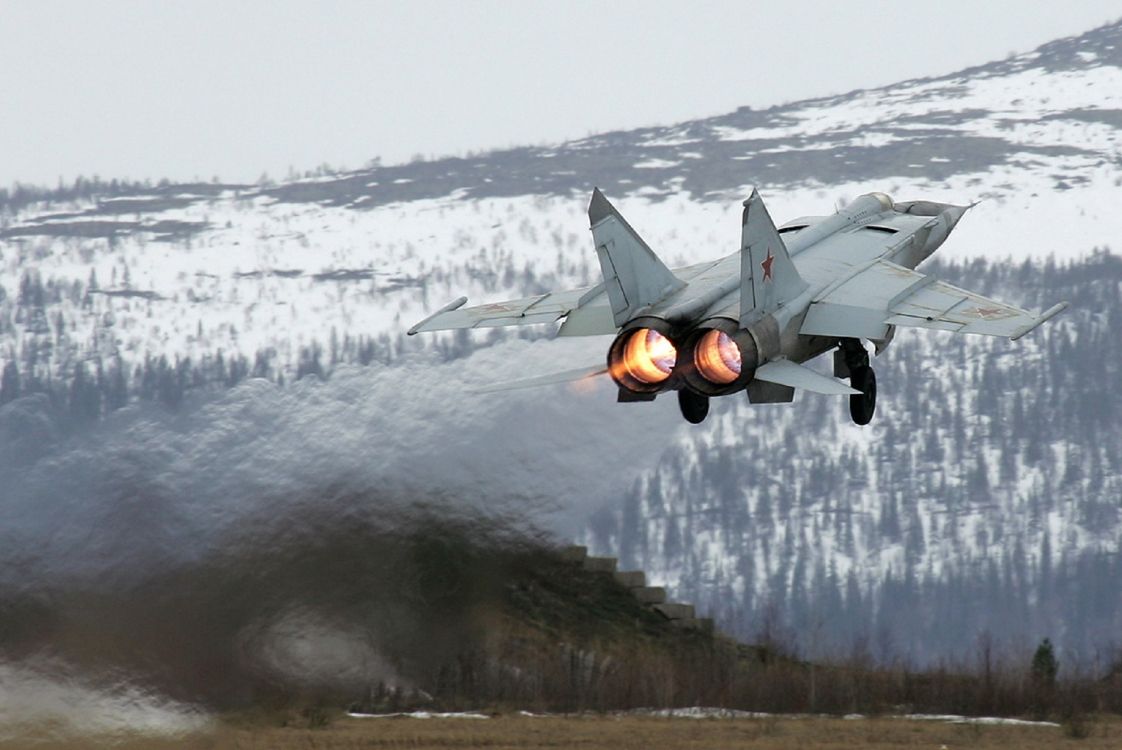 gray fighter plane flying over snow covered ground during daytime