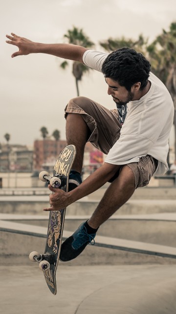 Image man in white t-shirt and brown shorts playing skateboard during daytime