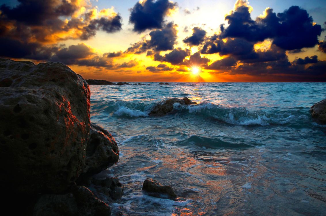 rocky shore under cloudy sky during sunset