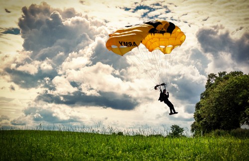 Image person in black jacket and pants riding yellow parachute under white clouds during daytime