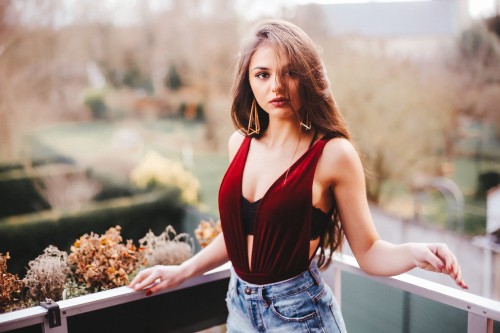 Image woman in red tank top and blue denim shorts standing beside white wooden railings during daytime