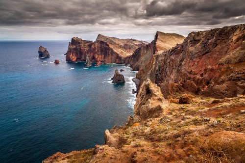 Image brown rocky mountain beside blue sea under blue sky during daytime