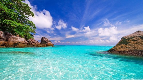 Image brown rock formation on blue sea under blue sky and white clouds during daytime