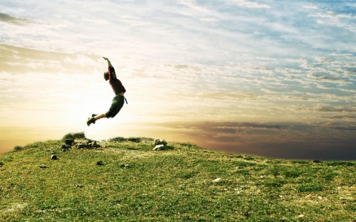 Image man in black shirt and black pants jumping on green grass field during daytime