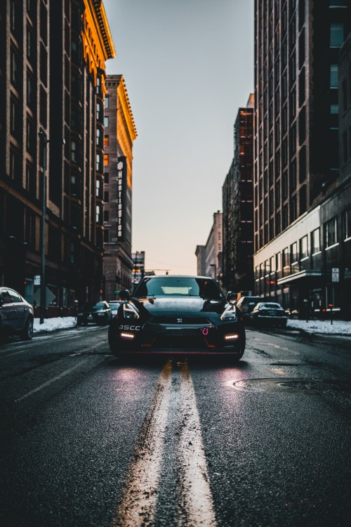 Image black sedan on road in between high rise buildings during daytime