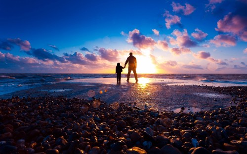 Image silhouette of man and woman standing on rocky shore during sunset