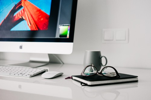 Image silver imac beside black framed eyeglasses and black ceramic mug on white table