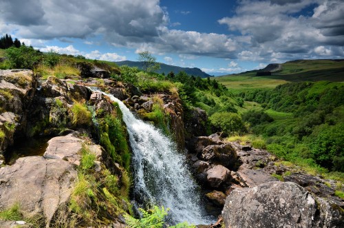 Image water falls on green grass field under white clouds and blue sky during daytime