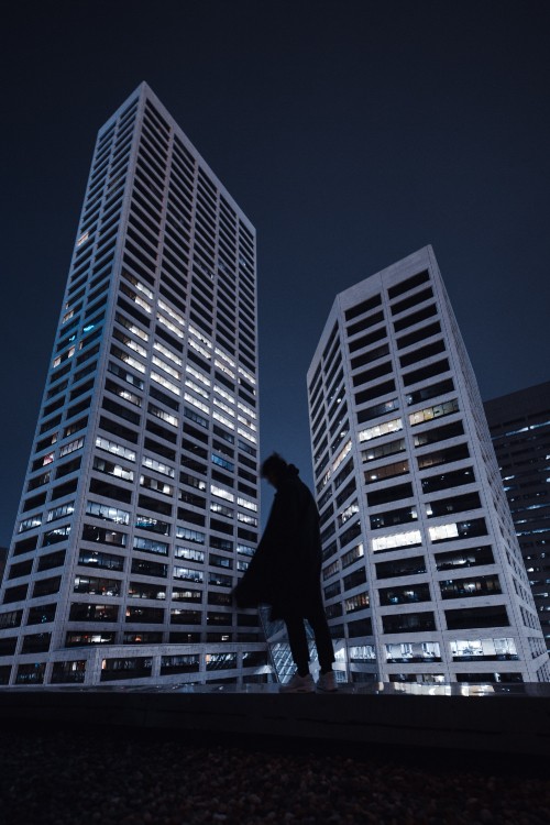 Image man in black jacket and pants standing in front of high rise building during night time