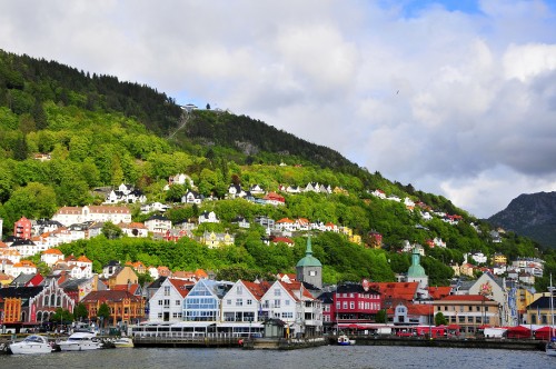 Image white and brown houses near green mountain under white clouds during daytime