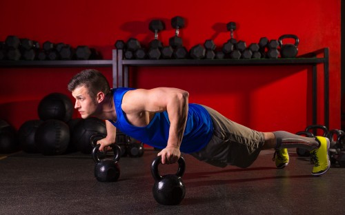 Image man in blue tank top and black shorts holding black kettle bell