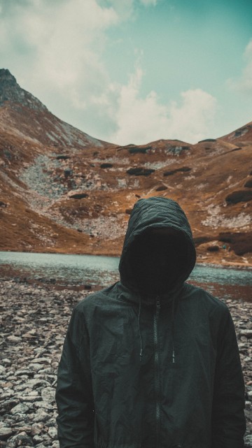 Image person in black hoodie standing on gray rocky ground during daytime