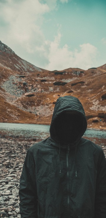 Image person in black hoodie standing on gray rocky ground during daytime