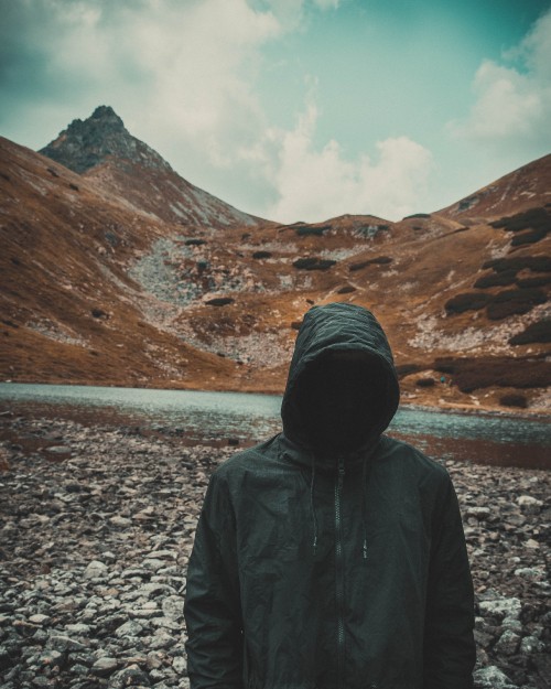 Image person in black hoodie standing on gray rocky ground during daytime