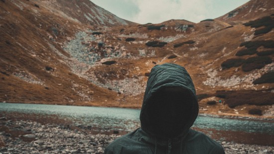 Image person in black hoodie standing on gray rocky ground during daytime