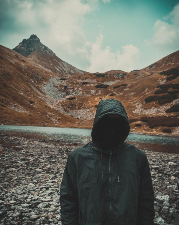 person in black hoodie standing on gray rocky ground during daytime