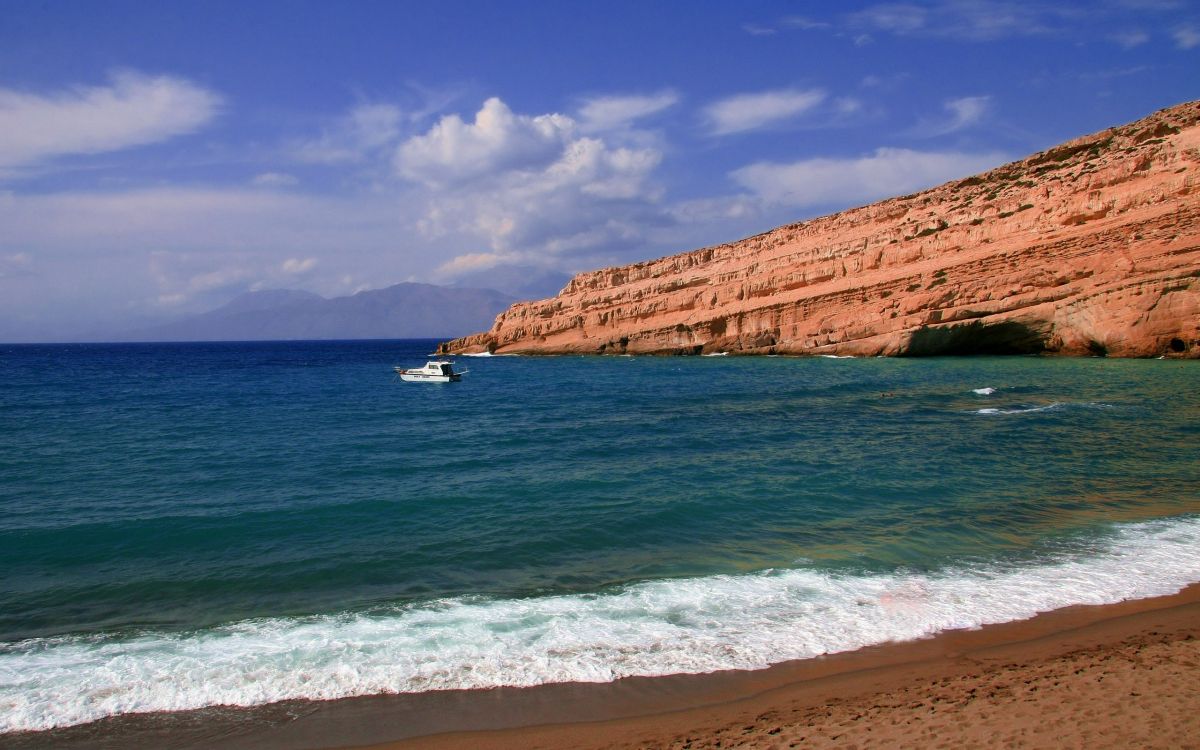 white boat on sea near brown rock formation under blue sky during daytime