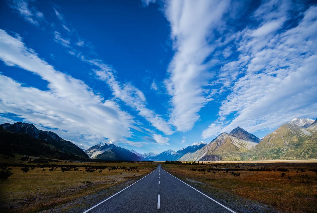 gray concrete road near mountain under blue sky during daytime