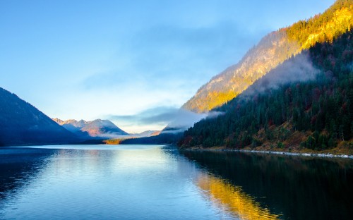 Image green and brown mountains beside body of water under white clouds during daytime