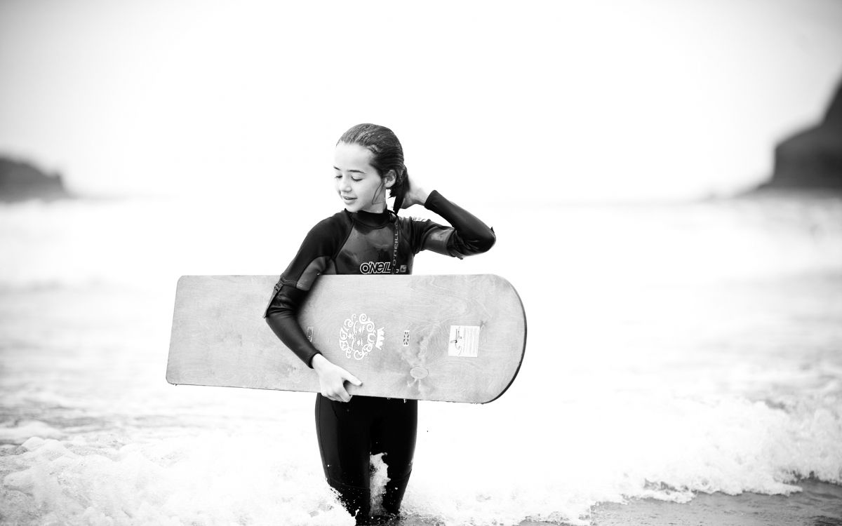 grayscale photo of man carrying a surfboard