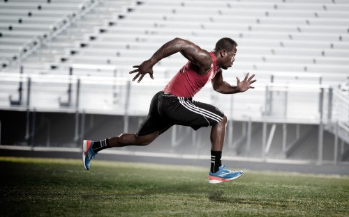 Image man in red tank top and black shorts running on green grass field during daytime