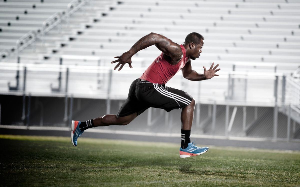 man in red tank top and black shorts running on green grass field during daytime