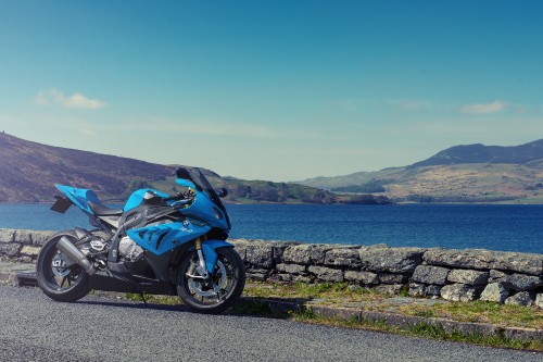 Image blue and black sports bike parked on gray concrete road near body of water during daytime