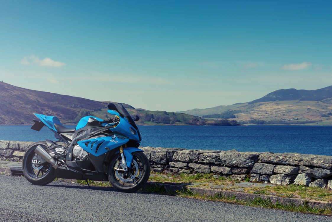 blue and black sports bike parked on gray concrete road near body of water during daytime