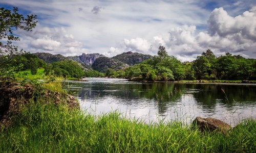 Image green grass near lake and mountain under white clouds during daytime